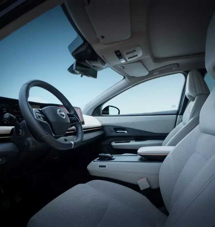 Interior do Nissan Ariya com bancos em pele clara, volante de couro com logótipo Nissan e duplo ecrã digital panorâmico no painel de instrumentos