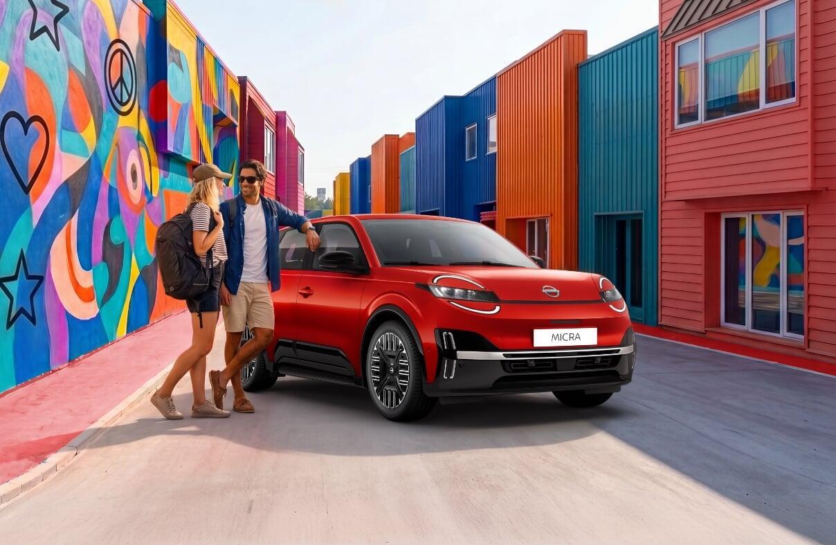 Nissan Micra elétrico vermelho estacionado em rua com casas coloridas; casal parado ao lado do veículo.