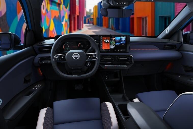 Interior do Nissan Micra elétrico mostrando painel digital, volante com logo Nissan e tela multimídia central, com mural colorido visível pelo para-brisa.