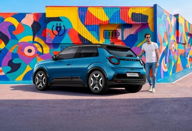 Nissan Micra elétrico azul visto de trás, estacionado diante de mural colorido com ícones de carregador e bateria; homem parado ao lado do carro.