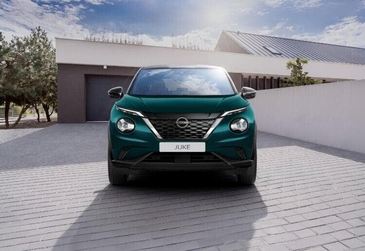 Nissan Juke verde, usado certificado, visto de frente. O carro está no exterior de uma moradia moderna. 