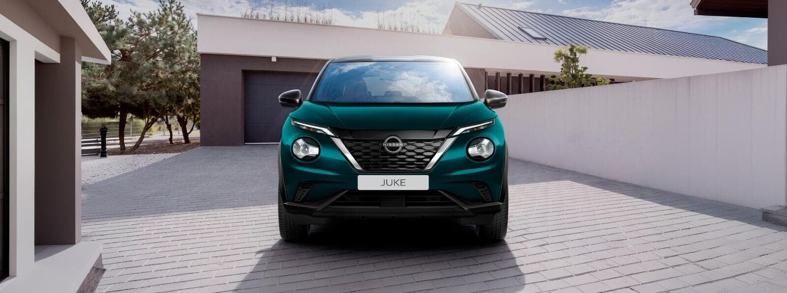 Nissan Juke verde, usado certificado, visto de frente. O carro está no exterior de uma moradia moderna. 